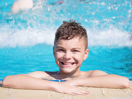 Close-up portrait of happy teen boy in the swimming pool at aquapark. Cute child having fun enjoyable time on vacation. Looking at camera.の写真素材