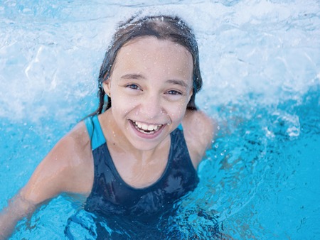 Close-up portrait of happy girl in the swimming pool at aquapark. Cute child having fun enjoyable time on vacation. Looking at camera.の写真素材