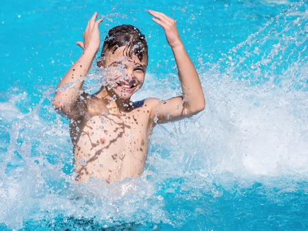 Happy teen boy jumping in the swimming pool at aquapark. Cute child having fun enjoyable time on vacation. He laughing and splashing water.の写真素材