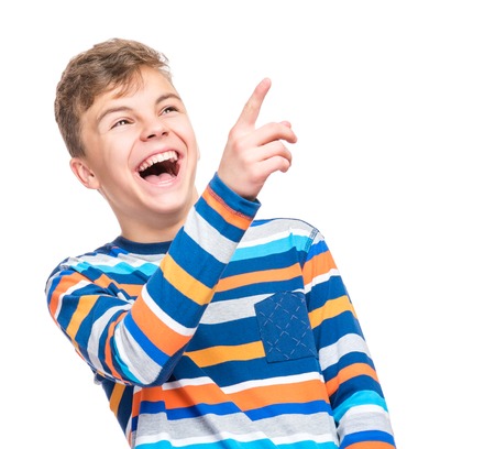 Emotional portrait of caucasian teen boy. Funny teenager pointing and looking upwards while laughing, isolated on white background. Handsome happy child pointing at copy space.の写真素材