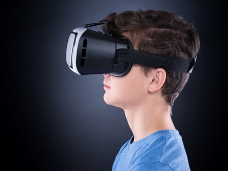 Happy teen boy wearing virtual reality goggles watching movies or playing video games. Cheerful smiling teenager looking in VR glasses. Profile of child experiencing 3D gadget technology - close up.の写真素材