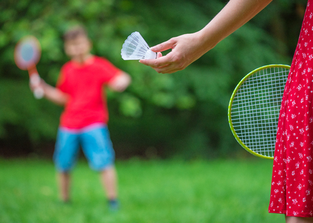 Teen boy and girl playing badminton in meadow with forest in background. Children with badminton rackets. Friends have fun in park - with soft selective focus on female hand with shuttlecock.の写真素材