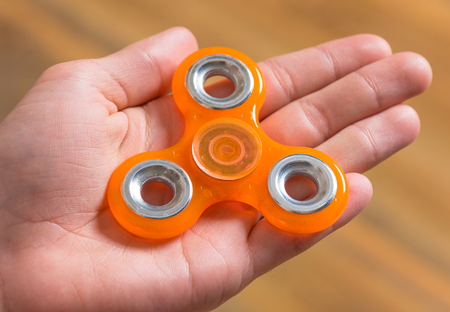 Male child hand holding popular fidget spinner toy - close up. Boy playing with a orange Spinner.の写真素材
