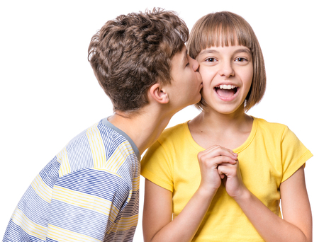 Friendship - teen boy kissing beautiful girl. Portrait of happy brother and sister, isolated on white background. Funny couple children - first love.の写真素材