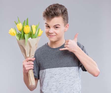 Teen boy with bunch of flowers on gray background. Smiling child with bouquet of tulips as a gift. Happy mothers or Valentines day!の写真素材