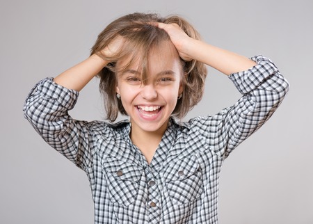 Close-up emotional portrait of caucasian little girl. Funny victory screaming teenager, on gray background. Lucky schoolgirl celebrating triumph, shouting with her hands up.の写真素材