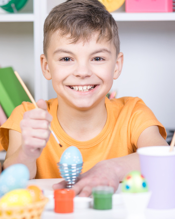 Cute boy painting eggs at home. Happy child preparing for Easter.の写真素材