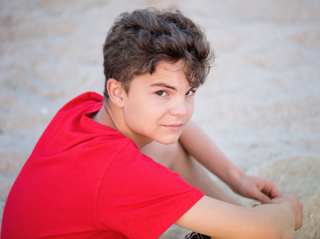 Teen boy on sand on beach - summer vacation, close-up portrait. Child looking up at camera.の写真素材