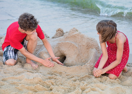 Happy girl and boy playing on sea shore at sandy beach during summer holiday. Cute children - brother and sister on vacation, outdoors.の写真素材