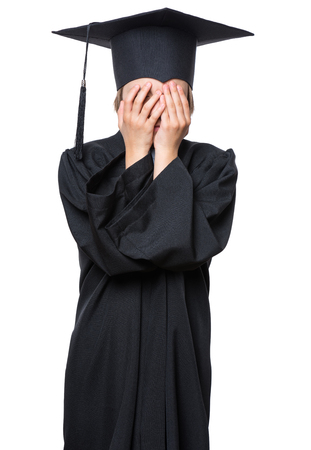 Sad crying disappointed graduate little girl student in black graduation gown with hat - isolated on white. Negative human emotion facial expression. Child back to school, educational concept.の写真素材