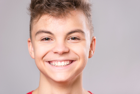 Close up emotional portrait of caucasian teen boy. Handsome smiling guy. Funny cut teenager on gray background. Happy child looking at camera.の写真素材