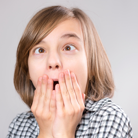 Silly girl making grimace - funny face. Child on gray background. Emotional portrait of caucasian teenager looking at camera.の写真素材