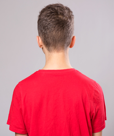 Beautiful caucasian teen boy wearing red t-shirton gray background. Child close-up of back view.の写真素材