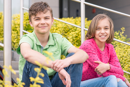Happy teenage boy and girl smiling while sitting on the stairs outdoors. Young sister and brother teens sitting on the stairs and looking at camera.の写真素材