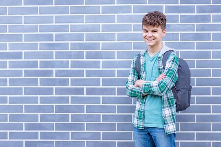 Schoolchild go to school with backpack. Smiling cute child - teen boy with bag against a brick wall outdoors. Childhood and Back to school concept.の写真素材