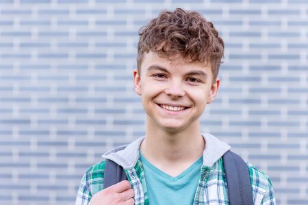 Schoolchild go to school with backpack. Smiling cute child - teen boy with bag against a brick wall outdoors. Childhood and Back to school concept.の写真素材