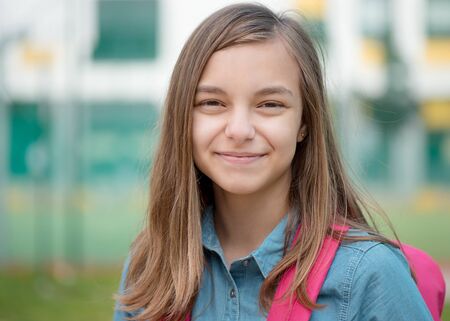 Portrait of beautiful student teenager schoolchild go to school with backpack. Cute child - teen girl with bag against the background of school. Back to school concept.の写真素材