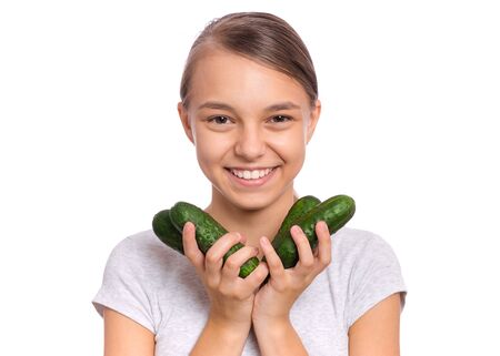 Portrait of beautiful young teen girl holding fresh green cucumbers, isolated on white background. Smiling pretty child with healthy raw vegetables in hands. Organic natural healthy food produce.の写真素材