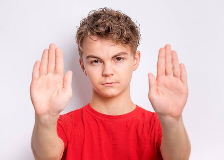 Teen boy doing stop sign with palm of hands, on grey background. Beautiful caucasian teenager making...