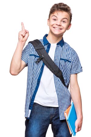 Portrait of cheerful teen boy with good idea. Cute schoolboy with school bag and books pointing up, isolated on white background.の写真素材