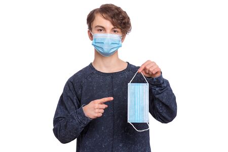 Concept of coronavirus quarantine. Child wearing medical protective mask to health protection from influenza virus, isolated on white background. Portrait of Teen boy holds protective face mask.の写真素材