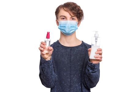 Concept of coronavirus quarantine. Child wearing medical protective mask, holds antibacterial antiseptic spray and soap for hands disinfection during flu virus outbreak. COVID-19. Teen boy on white.の写真素材