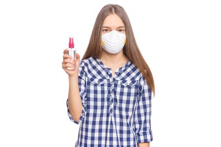 Concept of coronavirus quarantine. Child wearing medical protective mask with antibacterial antiseptic spray for hands disinfection during flu virus outbreak. COVID-19. Teen Girl isolated on white.の写真素材