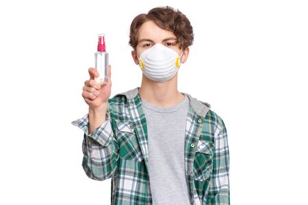 Concept of coronavirus quarantine. Child wearing medical protective mask with antibacterial antiseptic spray for hands disinfection during flu virus outbreak. COVID-19. Teen Boy isolated on white.の写真素材