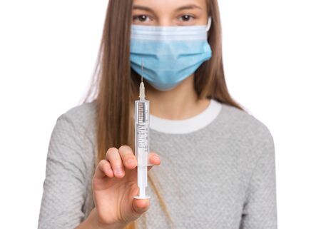 Concept of coronavirus quarantine. COVID-19. Child wearing medical face mask to health protection from influenza virus, isolated on white. Teen girl holds syringe with vaccine. Selective focus.の写真素材