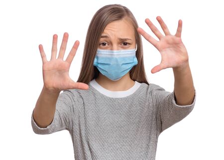 Concept of coronavirus quarantine. Child wearing medical protective face mask during flu virus, making stop gesture. COVID-19 - home self isolation. Teen Girl doing stop sign, isolated on white.の写真素材