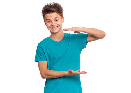 Handsome teen boy shows something in his hands and looking at camera, isolated on white backgroundの写真素材