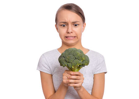Happy beautiful young teen girl holding perfect product for dieting green broccoli, isolated on white backgroundの写真素材