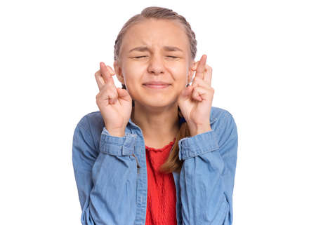 Happy teenage girl looking very happy holding fingers crossed for good luck, isolated on white backgroundの写真素材