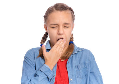 Beautiful teenage girl yawns covering her mouth with hand, isolated on white backgroundの写真素材