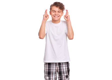 Handsome teen boy looking very happy holding fingers crossed for good luck, isolated on white backgroundの写真素材