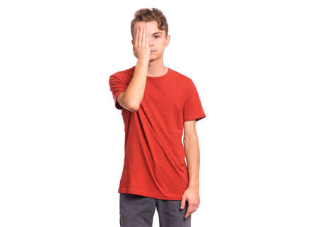 Sad handsome teen boy looks with one eye while covering his other eye with his hand, isolated on white backgroundの写真素材
