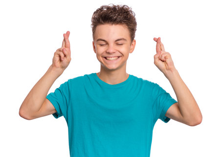 Handsome teen boy looking very happy holding fingers crossed for good luck, isolated on white backgroundの写真素材