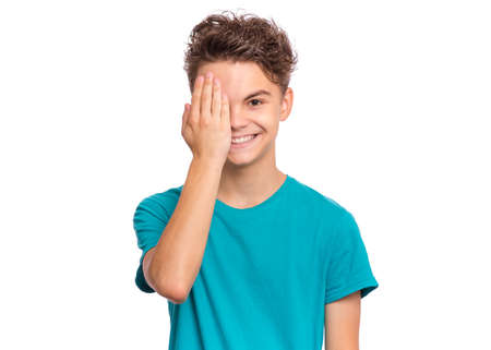 Handsome teen boy looks with one eye while covering his other eye with his hand, isolated on white backgroundの写真素材