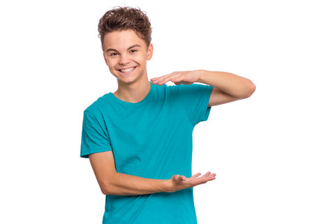 Handsome teen boy shows something in his hands and looking at camera, isolated on white backgroundの写真素材