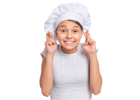Teen girl in chef hat, keeping fingers crossed and making wish, isolated on white background.の写真素材