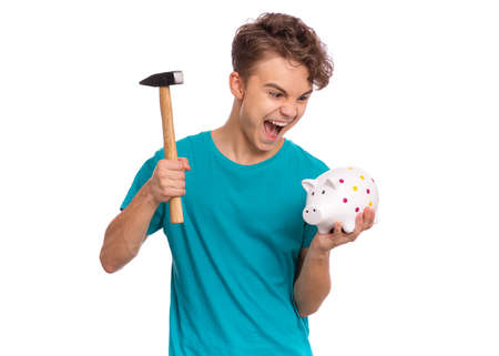 Portrait of teen boy holding Piggy Bank and Hammer. Cute caucasian young teenager isolated on white background. Saving Money concept. Crazy funny child about to break his piggybankの写真素材