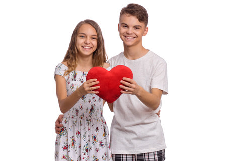 Happy teen boy and girl standing together, holds plush heart in hands. Hugging smiling teenagers with symbol of love, family, hope. Portrait of sweet young couple in love. Friendship and love conceptの写真素材