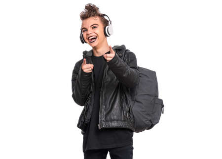 Portrait of teen boy student in headphones with spooking make-up holds bag, isolated on white background. Teenager with backpack in style of punk goth dressed in black. Problems of transitional ageの写真素材