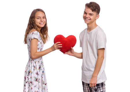 Happy teen boy and girl standing together, holds plush heart in hands. Hugging smiling teenagers with symbol of love, family, hope. Portrait of sweet young couple in love. Friendship and love conceptの写真素材