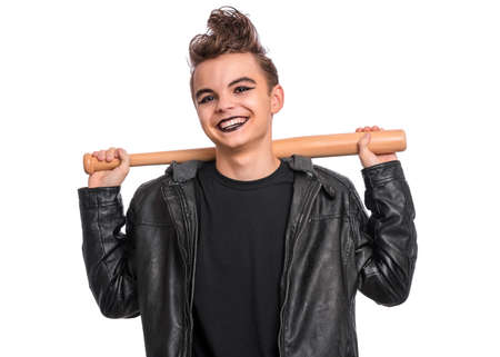 Rebellious teen boy dressed in black, isolated on white background. Young teenager in style of punk goth wearing leather jacket, holding wooden bat. Problems of transitional ageの写真素材