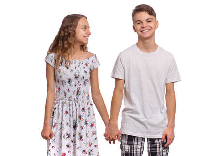 Portrait of smiling teen boy and girl holding hands together. Happy children in casual clothes, isolated on white background. Teenagers looks at camera. Friendship and love conceptの写真素材