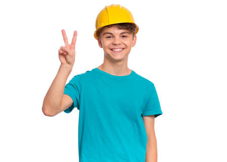 Portrait of confident smiling teen boy wearing yellow hard hat, isolated on white background. Beautiful student caucasian young teenager in helmet looking at cameraの写真素材