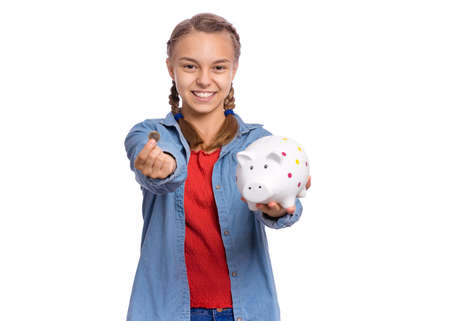 Beautiful teenage girl holds a piggy bank and a coin in her hands, isolated on white backgroundの写真素材