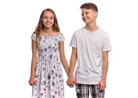 Portrait of smiling teen boy and girl holding hands together. Happy children in casual clothes, isolated on white background. Teenagers looks at camera. Friendship and love conceptの写真素材