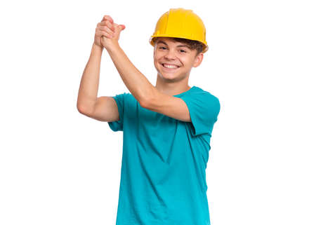Portrait of confident smiling teen boy wearing yellow hard hat, isolated on white background. Beautiful student caucasian young teenager in helmet looking at cameraの写真素材